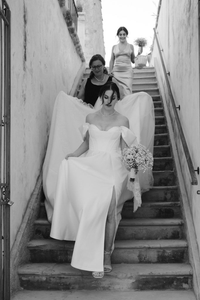 Braut steigt mit Trauzeugin und Mutter eine Treppe in Sizilien hinab zur Hochzeit