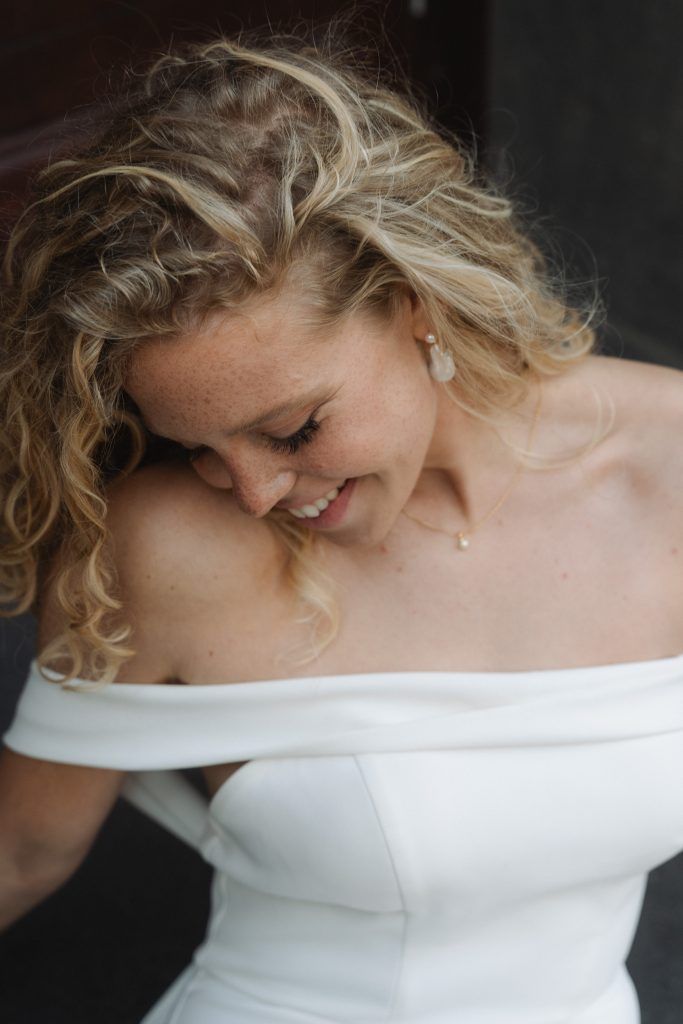 Lächelnde Braut im weißen Hochzeitskleid bei einem natürlichen Porträt